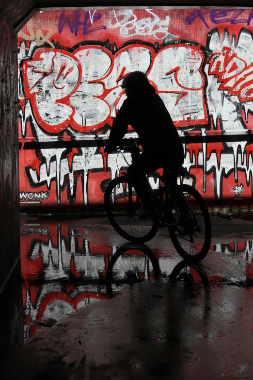 there is a man riding a bike by a wall covered in graffiti