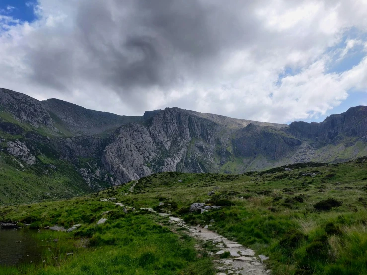 grassy area with rock and water surrounded by mountains