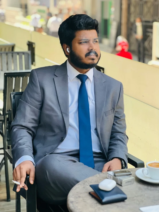 man in a suit sitting outside eating a cup of coffee