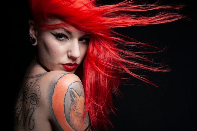 a young woman with bright red hair and tattoos, against a black background