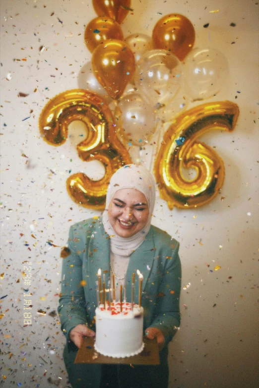 a woman holding up a cake with golden balloons