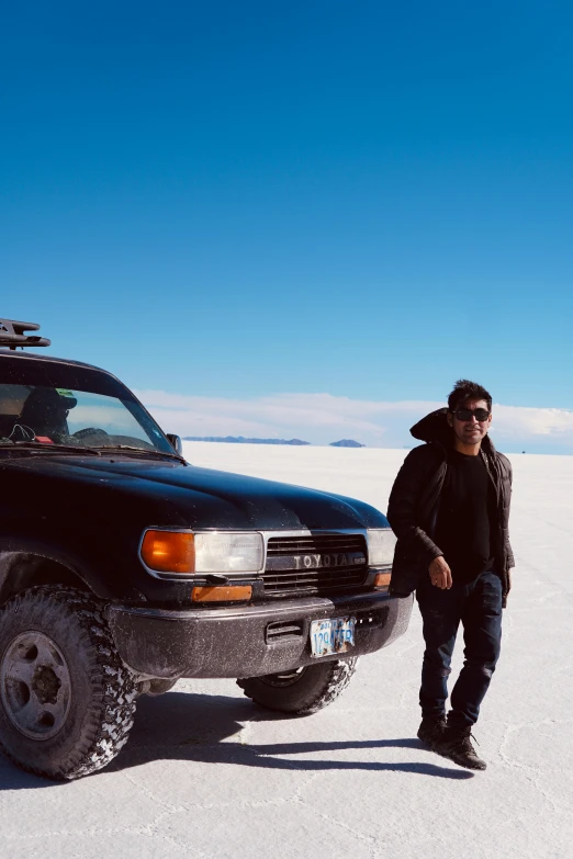 a man stands next to a black vehicle in the snow