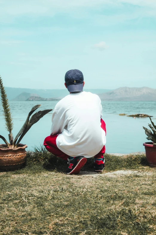 man sitting on grass and looking at ocean