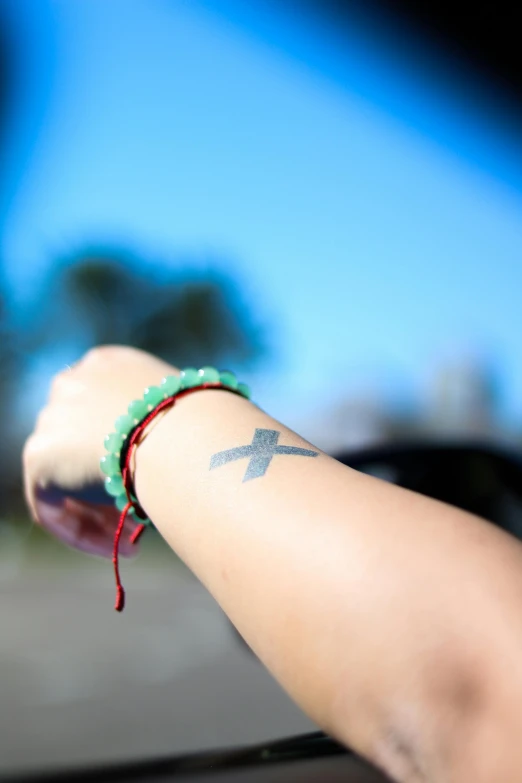 the cross tattoo on the arm of someone wearing a celet