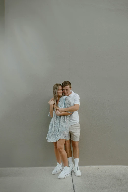 a young man and woman hugging each other while standing against a wall