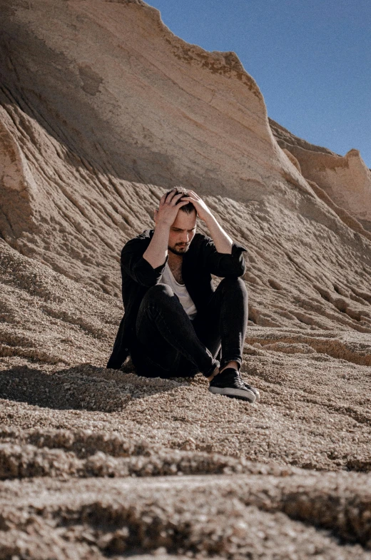 a man sitting in the sand near rocks