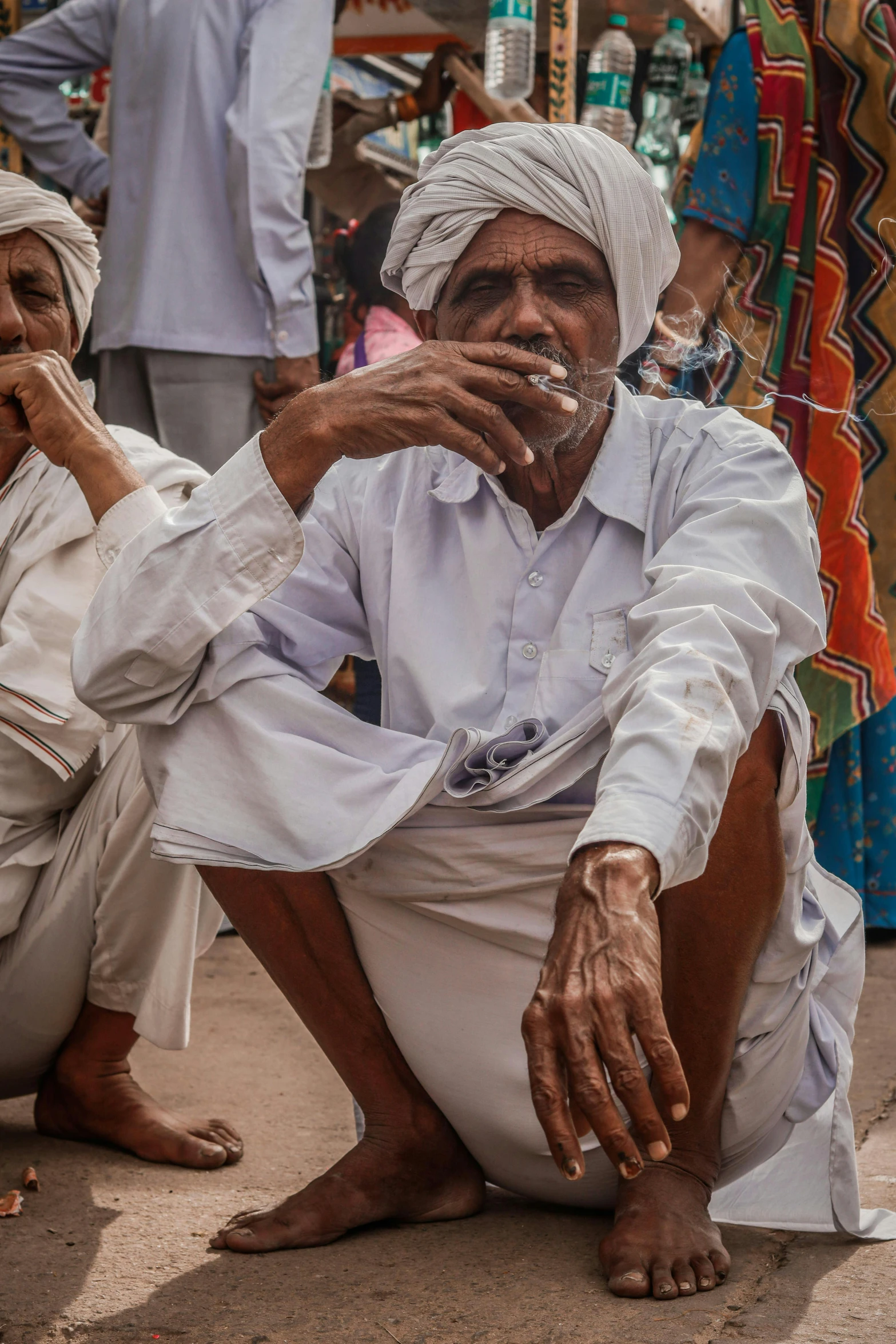 an old man sitting on the ground and smoking a cigarette