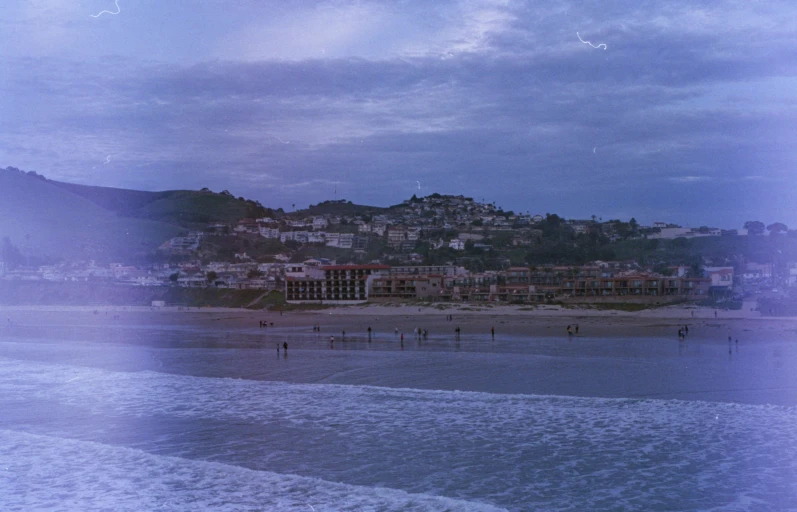 people stand in the surf at a beach near a city