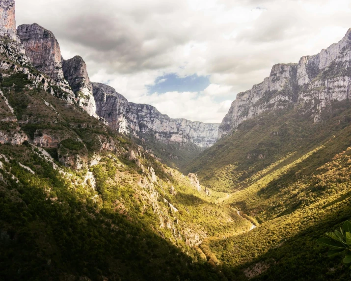 a mountain landscape with green valley, hills and clouds in the distance