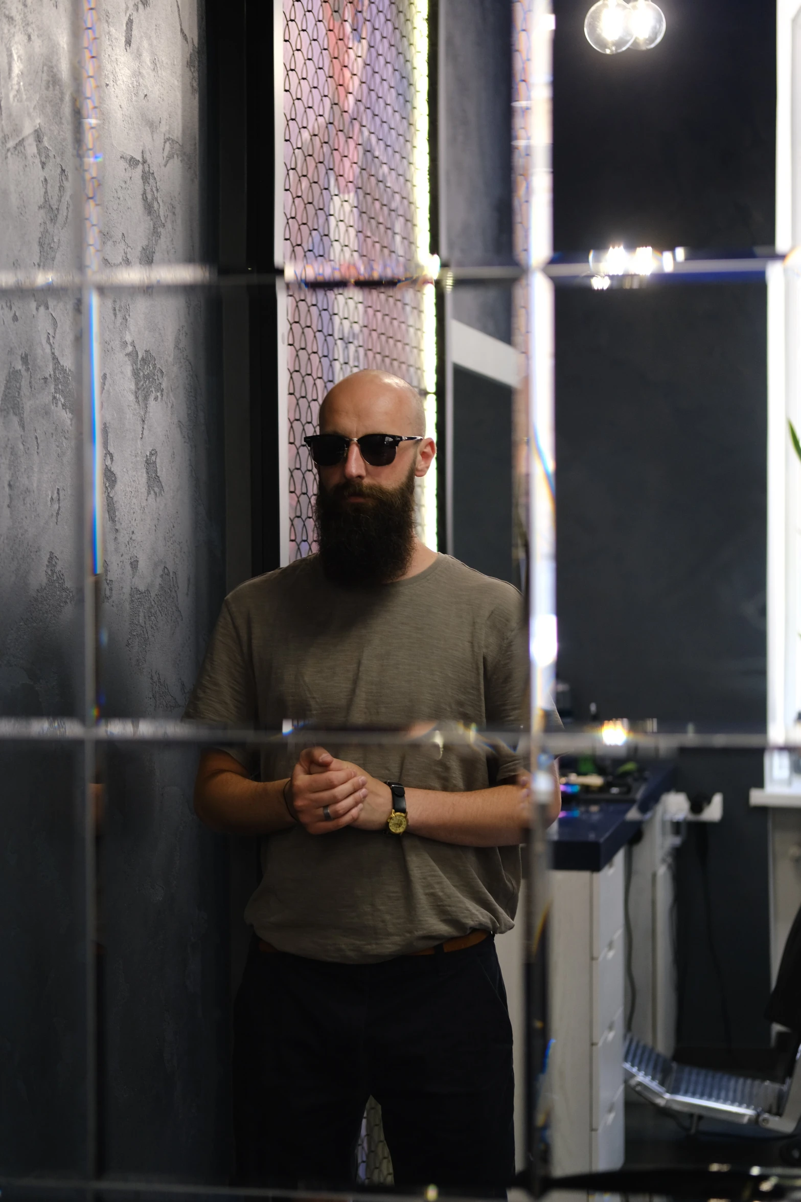 a man with glasses standing next to a wall and wearing a watch