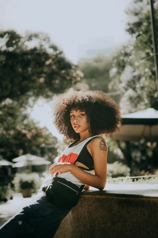 a young woman with an afro sitting in front of a tree