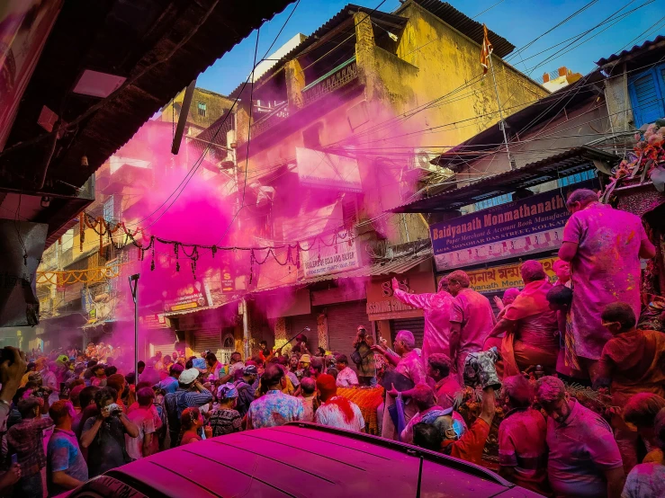 people walking through a street with pink powder coming out of the building