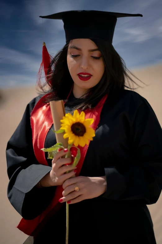 a woman in graduation gown holding a sunflower