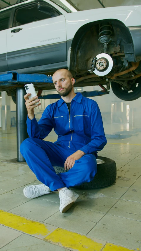 man in blue jumpsuit under white car taking selfie