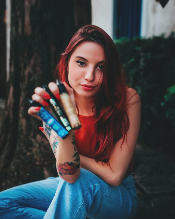 a girl sitting in the woods holding four different colors of lipstick