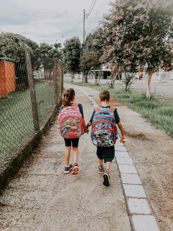 two children are walking down the pathway with backpacks