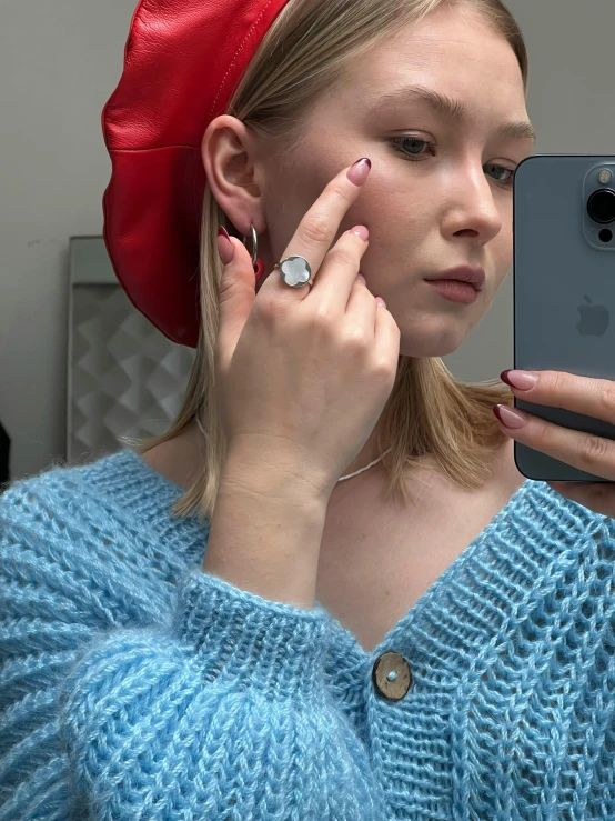 a woman wearing a red hat is looking into the mirror with her finger on her thumb