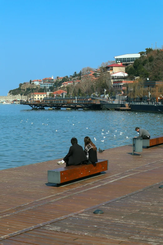 two people sitting on top of a bench next to the water