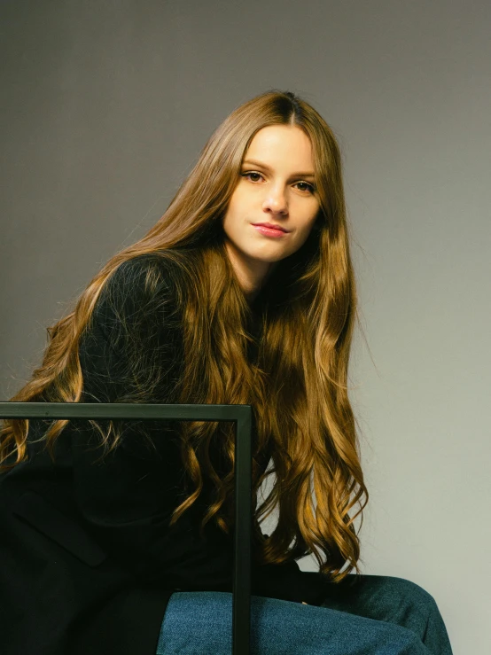 a woman with long, wavy hair is sitting on a chair