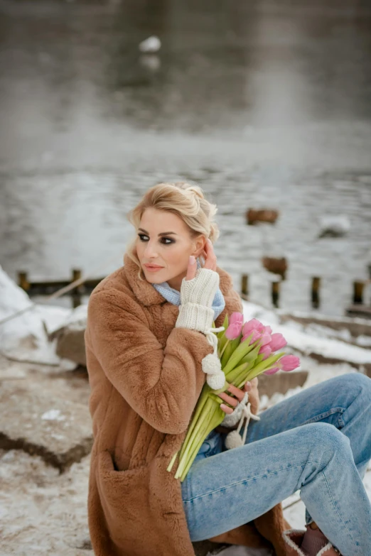 the beautiful blonde woman is sitting on the snow bank with flowers