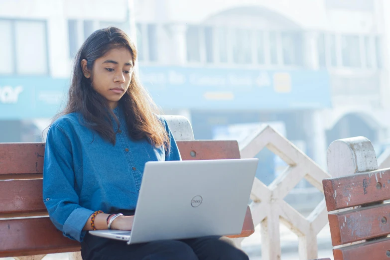 a young woman sits outside while working on her laptop