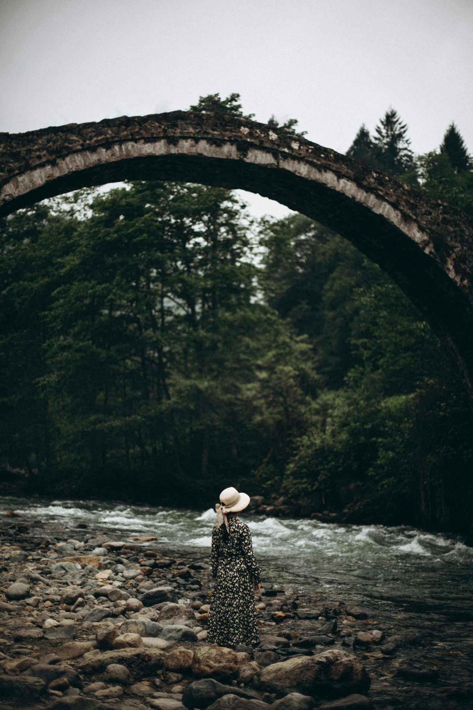 a woman standing in the water under a stone arch