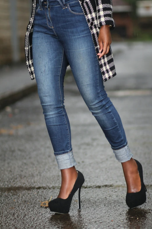 a woman in black and white blazer, jeans and heels standing on street