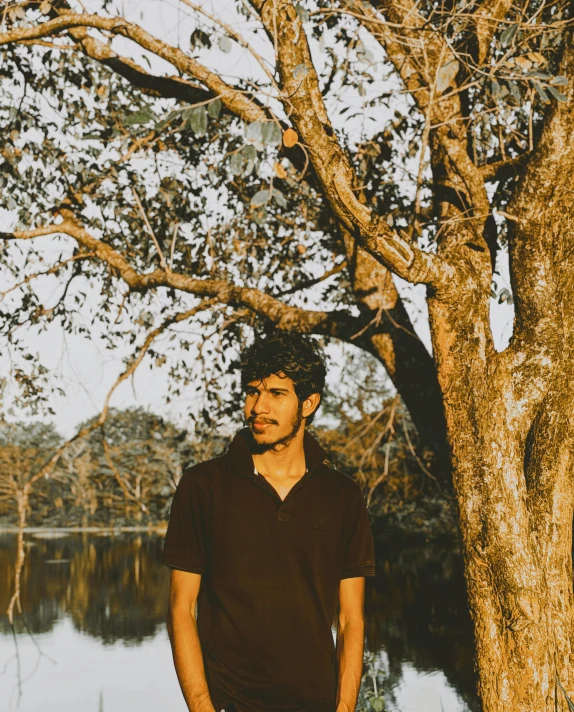 a guy standing next to a tree near water