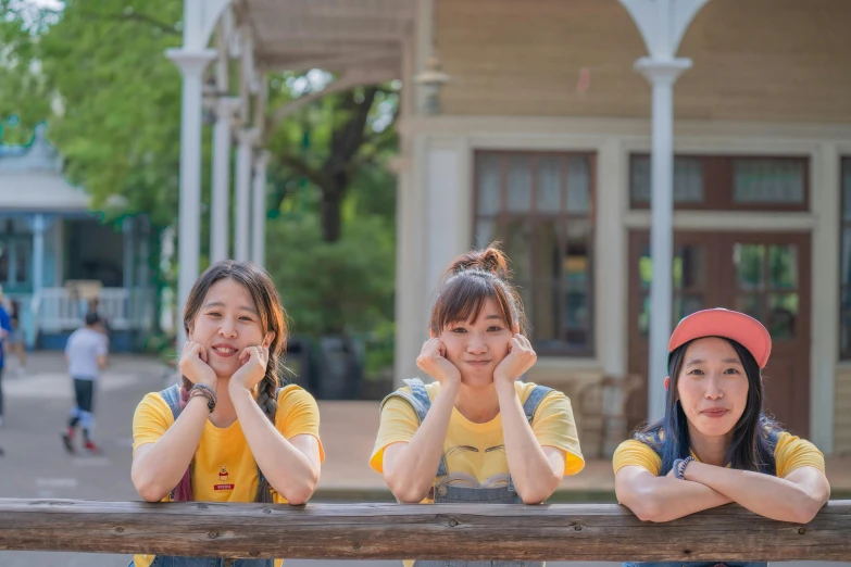 three young women leaning on a rail in front of a building