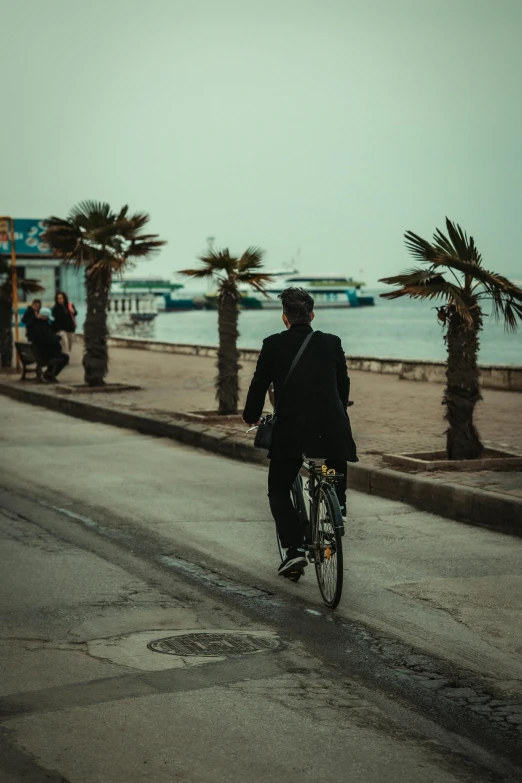 man in suit on bicycle passing next to sidewalk and beach