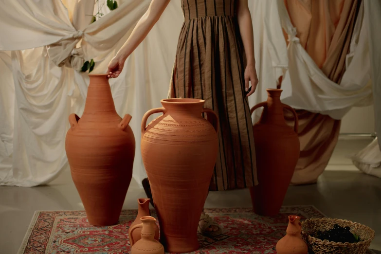 a woman is posed with several vases behind her