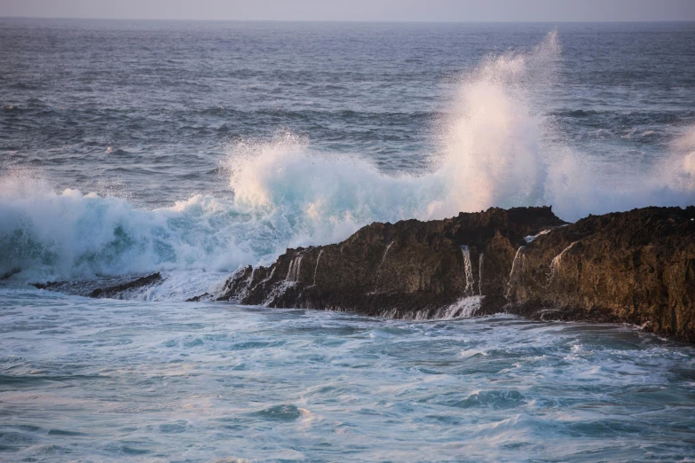 a wave crashing against some rocky cliffs near the sea