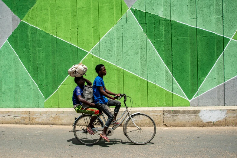 two people on a bike by a green and grey wall