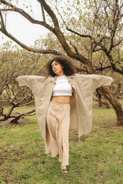 a young woman in a beige trench coat and high waisted trousers