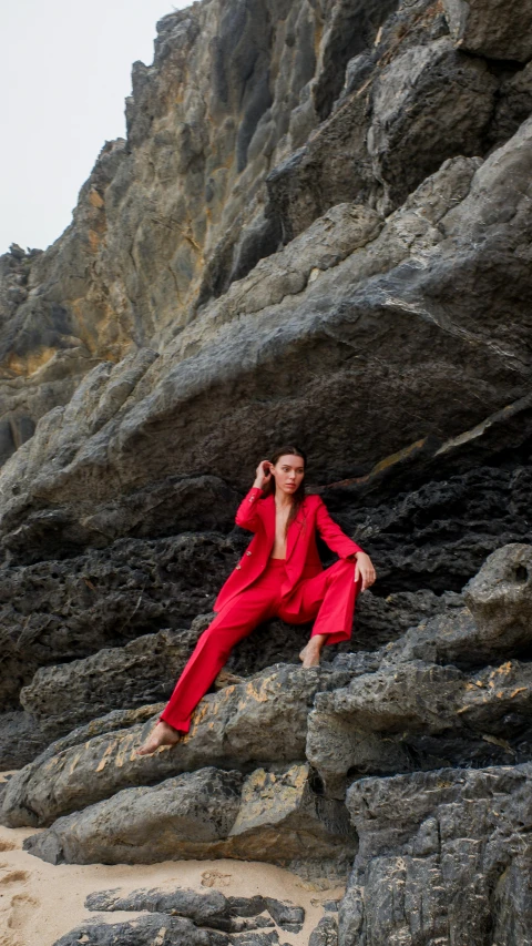 a woman sitting on the rocks with a red suit