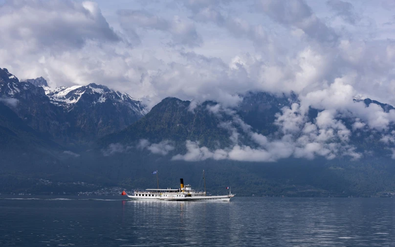 a boat with clouds floating around near mountains