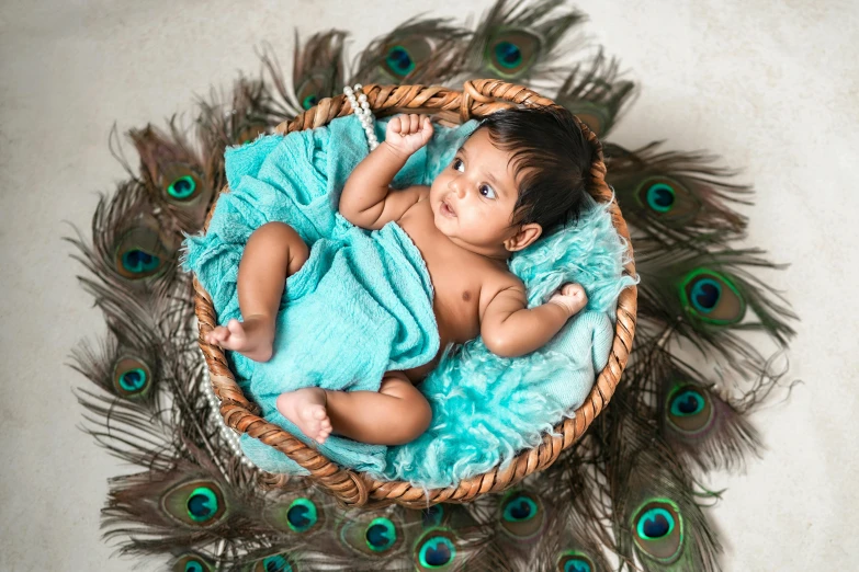 a baby wrapped in a blue towel laying on a peacock feather