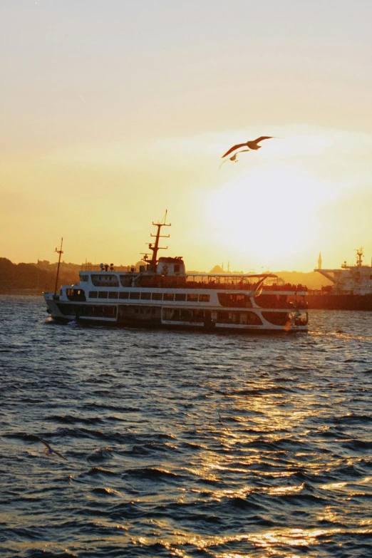 a cruise boat and a small ship in the water at sunset