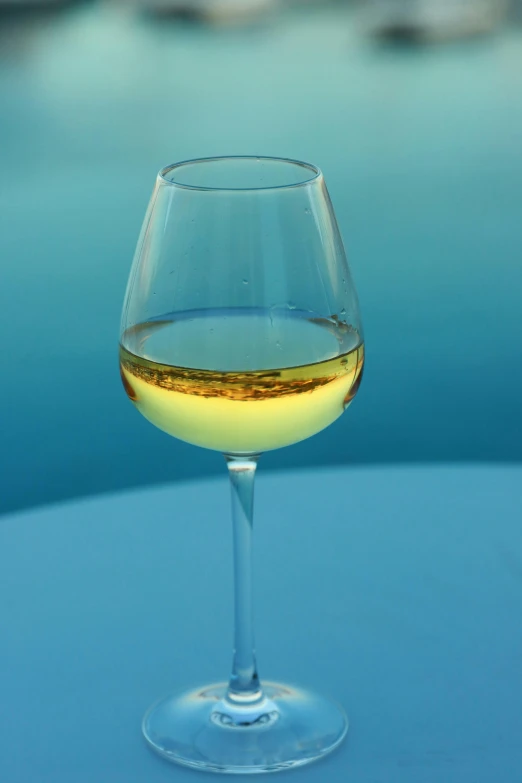 a wine glass filled with yellow wine sitting on top of a table