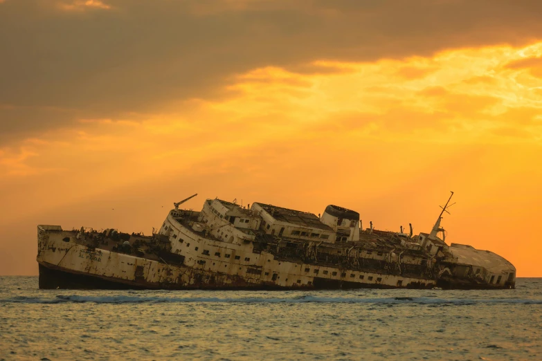 an old ship sitting on top of the water under a sunset