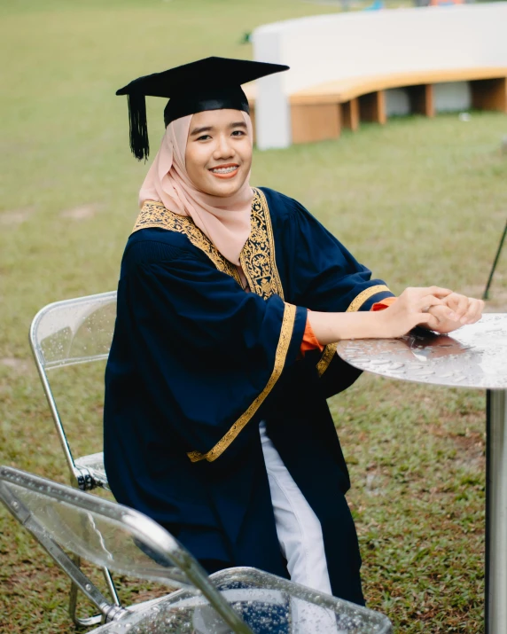 a young man dressed in graduation gown sitting at a table