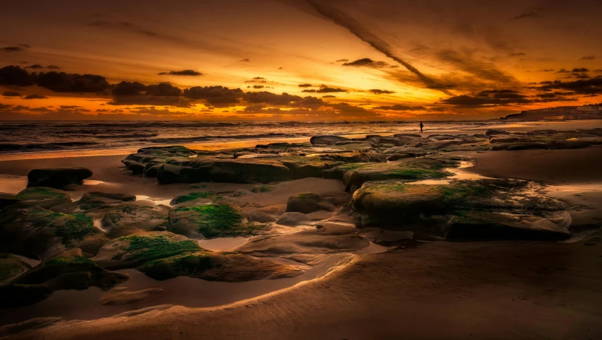 a beautiful sunset over some beach rocks and a long thin line of clouds