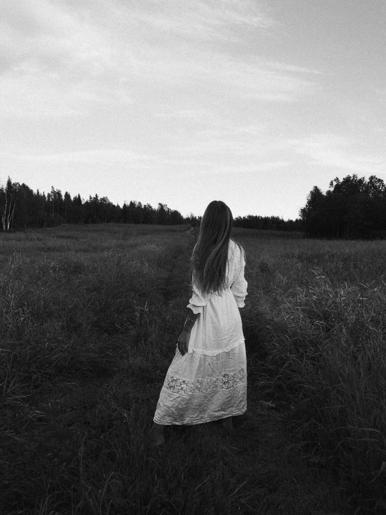 a woman in white dress walking through field at night