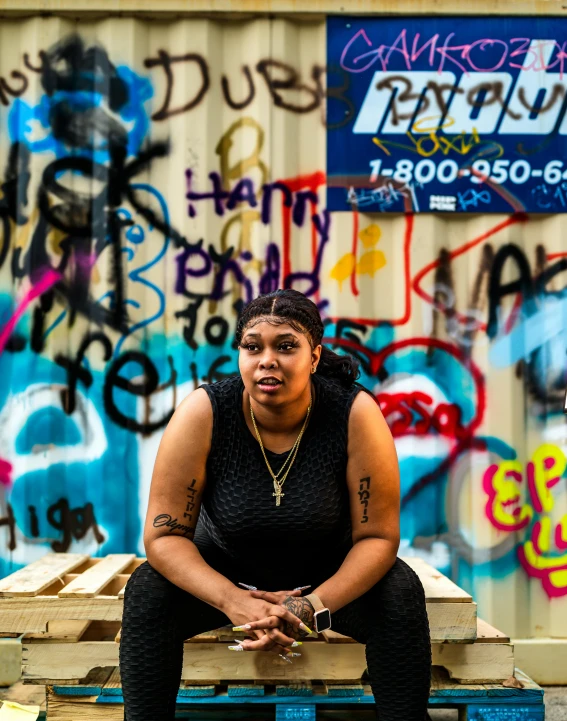 a black woman sits on a blue bench covered in graffiti