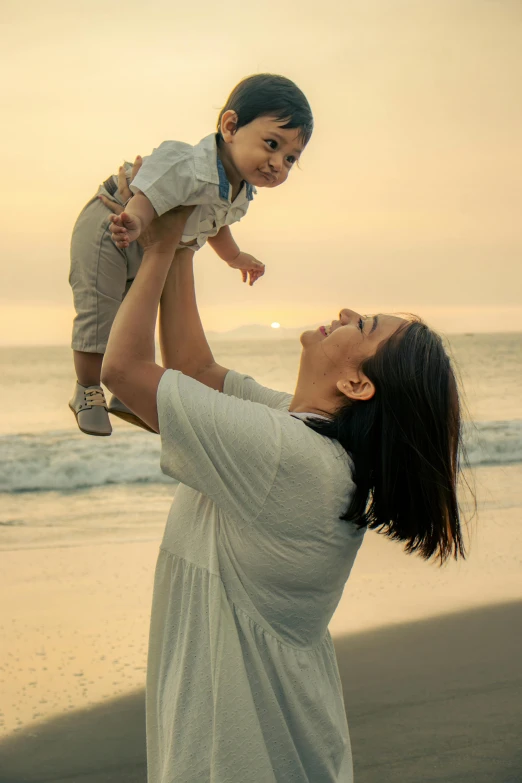 the mother holds her toddler up over his shoulder as he stands on the beach