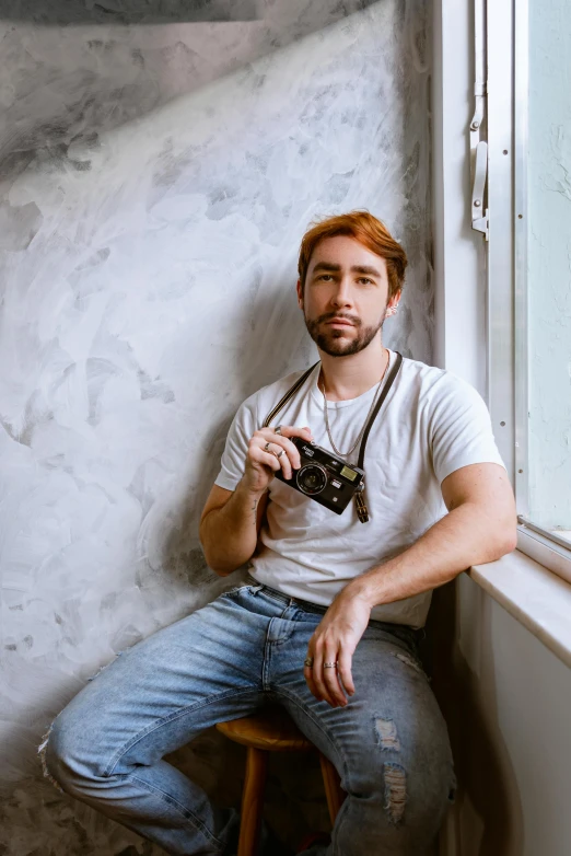 a man holding a camera sitting on a stool