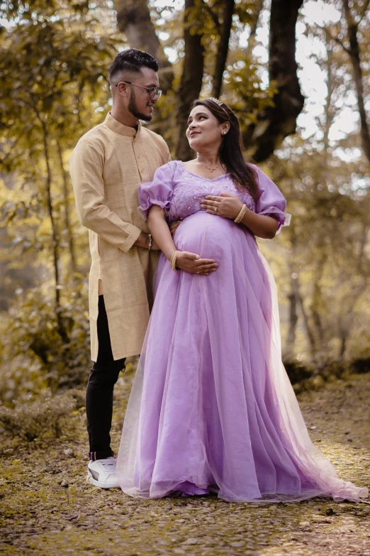 pregnant couple cuddling under a tree while dressed in clothes