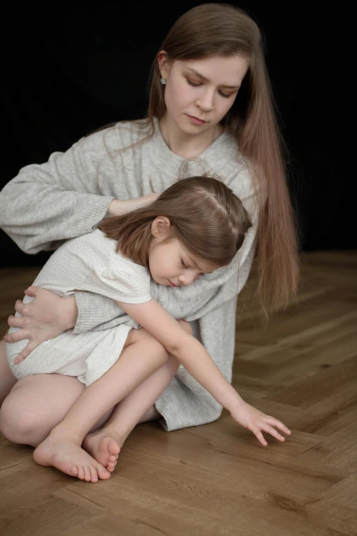 a woman kneeling next to a little girl on top of a wooden floor