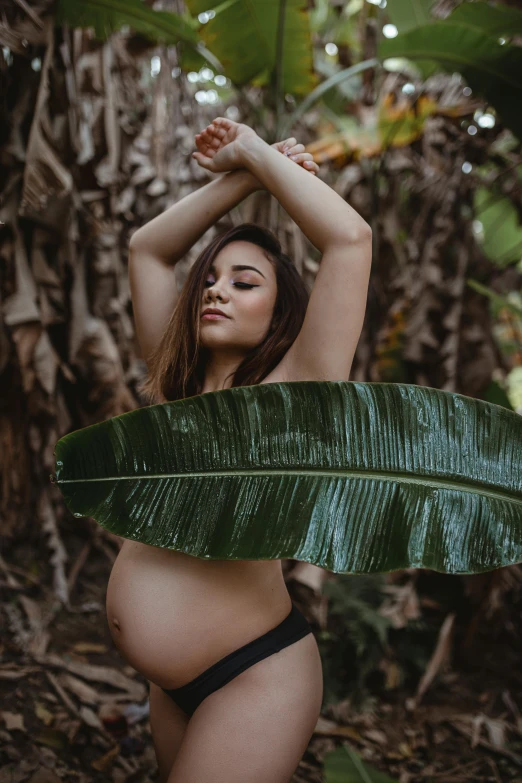 a woman in a black bikini is standing under a big leaf