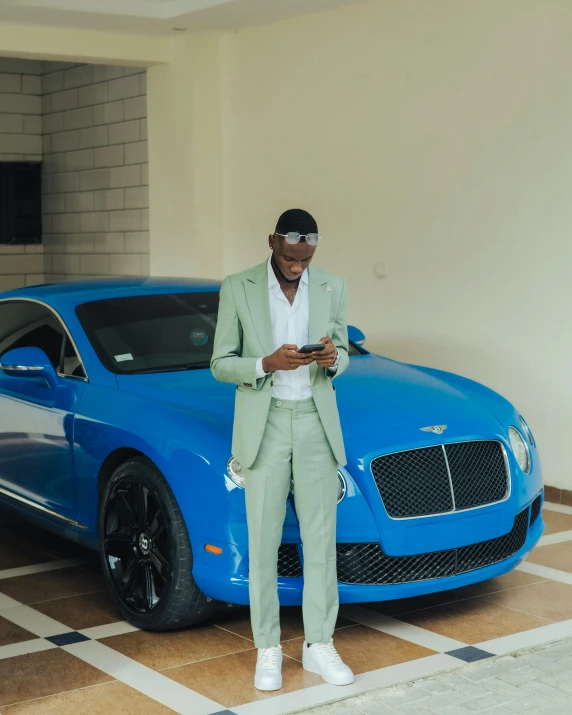 a man in green pants and a white shirt standing by a blue car